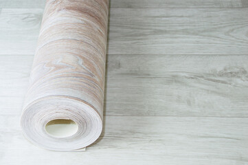 Rolled up roll of beige linoleum with wood texture white wood floor. Home renovation and improvement.