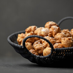 Basket of mini eclairs on gray background. Delicate French profiteroles dessert sprinkled with powdered sugar. Fresh puff pastry. Sweet delight. Soft focus. Side view. Copy space.
