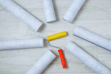 Gray textured wallpaper in rolls lying in the shape of a circle and roller closeup. White wooden background.
