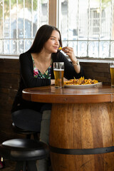 restaurant with wooden tables a young woman with long hair, eating a snack and drinking a glass of beer, lifestyle