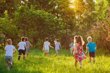 Obraz premium A group of happy children of boys and girls run in the Park on the grass on a Sunny summer day.