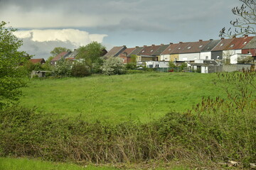 Rang&eacute;e de maisons derri&egrave;re une prairie sous un ciel d'orage &agrave; Ecaussinnes d'Enghien en Hainaut 