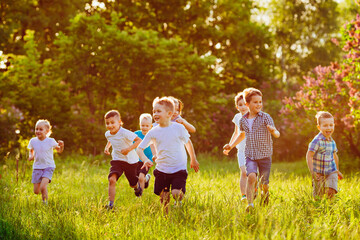 Fototapeta premium A group of happy children of boys and girls run in the Park on the grass on a Sunny summer day.