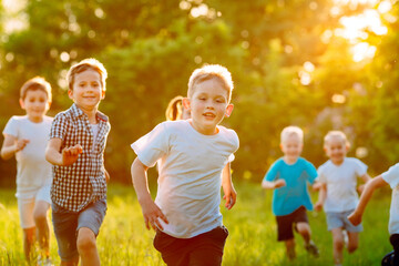 Fototapeta na wymiar A group of happy children of boys and girls run in the Park on the grass on a Sunny summer day.