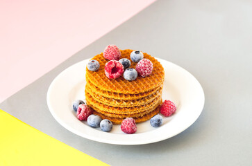 Traditional waffles with caramel and berries on white plate on geometric background. National Waffle Day. Trendy colors 2021. Creative copy space.