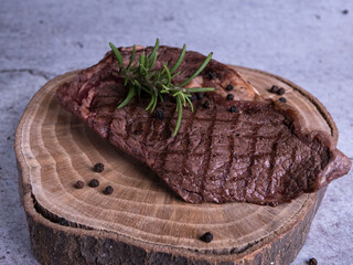 Sous-vide grilled beef steak with herbs in cast-iron skillet on wooden plate. Grey background with copy space