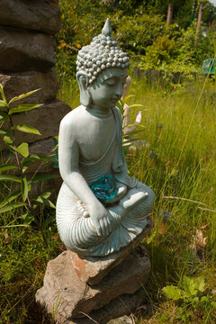 Blue-gray buddha sitting on a heap of stones. He has a turquoise glass stone on his lap. His hand gesture is called Bhumisparsha Mudra and means touching the earth.