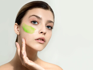 Young woman applying green face gel cream or facial mask at her face. Beauty model with perfect fresh skin and long eyelashes cares about her skin at home. 