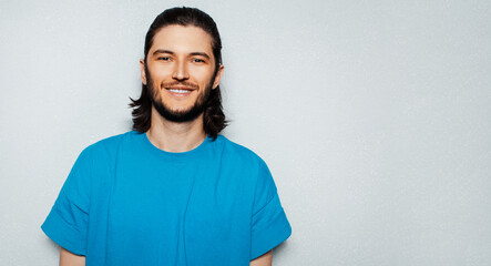 Portrait of young smiling man with long hair in blue shirt on textured background of grey  with copy space.