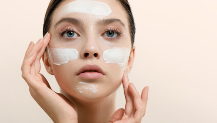 Young woman applying face cream or facial mask at her face. Beauty model with perfect fresh skin...