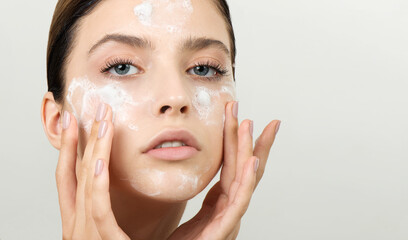 Beautiful young girl cleansing face with cosmetic facial skincare foam, gel or soap. Woman hame SPA...