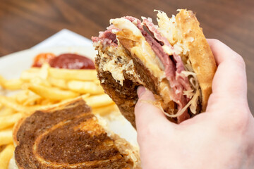 A patron hold a Rueben sandwich in one hand with the other half of sandwich and french fries...