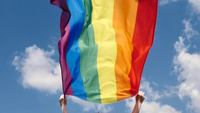Flag Rainbow LGBT Communite in a month of dignity or a parade on a background of blue sky with clouds in sunny weather. Person, woman, lesbian holds in her hands