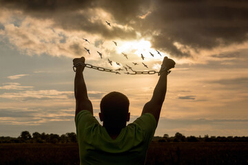 A man breaks the chain that crumbles into birds against the backdrop of a sunny sunset.
