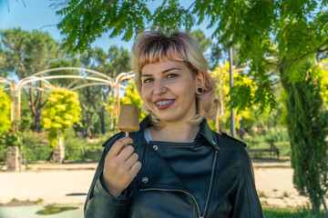 mujer joven con chaqueta negra sujetando un helado , chica comiendo un helado en el parque, chica...
