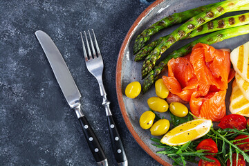 Salad with asparagus, grilled halloumi cheese, salmon fillet, tomatoes, arugula and green olives. Top view