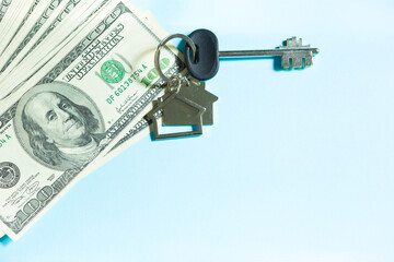 Home key with a keychain on a stack of $ 100 bills on a blue background. Purchase of an apartment, house, real estate, business, mortgage and housing loan from bank, savings, cash, moving. Copy space
