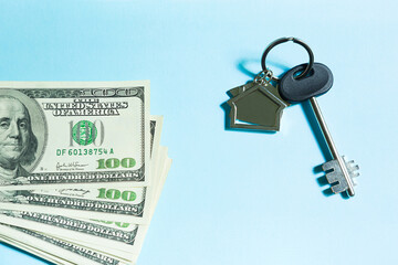 Home key with a keychain on a stack of $ 100 bills on a blue background. Purchase of an apartment, house, real estate, business, mortgage and housing loan from bank, savings, cash, moving. Copy space