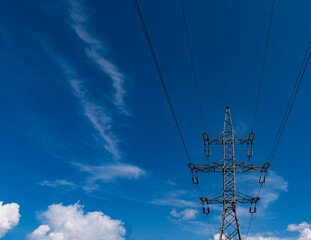 High-voltage pole against a blue sky with beautiful white clouds. Overhead power line wires. Bottom...