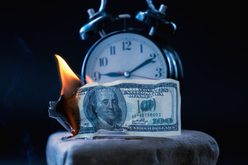 Burning US Dollar bills and the clock as symbol of lost time and opportunities. Selective focus on...