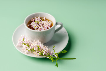 Floral spring composition and a mug of tea on a green background, top view, copy space