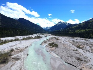 drone view of alpine valley with huge stony stream bed and grey-blue water creek, green mountains...