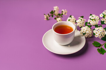 Floral spring composition and a mug of tea on a purple background, top view, copy space