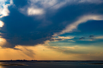 Fototapeta premium Dramatic clouds over the river and the city in the background. Clouds at sunset over river