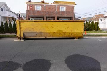 Old long yellow dumpster on an asphalt street in front of a brick building being renovated