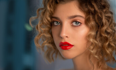 Portrait of Beautiful Fashion Model with Wavy Curly Hair and Colored Make-up with red Lips is posing front the Window. Make up and Hair. Haircare concept.