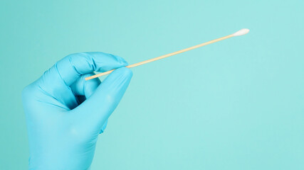 One Cotton stick for swab test in hand with blue medical gloves or latex glove on mint green or...