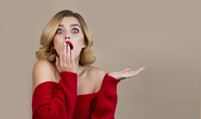 Portrait of beautiful young woman wearing red sweater with perfect young skin and professional makeup with scarlet red lips is shocked by discounts. Winter seasonal beauty concept.