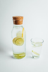 Refreshing glass of water, a bottle with a slice of lemon and lime inside on white background