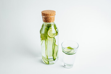 Refreshing glass of water, a bottle with a slice of cucumber and lime inside on white background