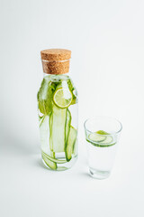 Refreshing glass of water, a bottle with a slice of cucumber and lime inside on white background