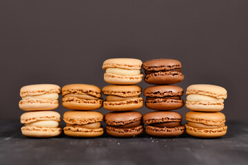 Brown, beige and cream colored French macarons stacked up in front of dark background