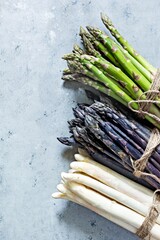 Raw white, purple, green asparagus on a blue background. Raw food concept.