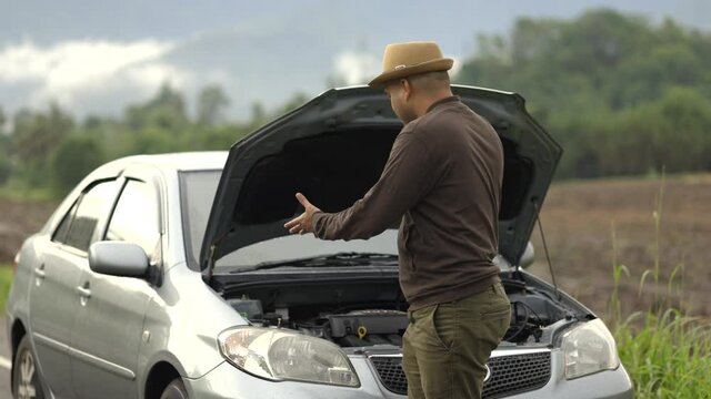 Asian man has  broken down car on the road he talking on phone to call someone to help or mechanics car service. Emergency assistance service