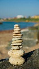 Fototapeta na wymiar Stone pyramid on sea stone coast near to sand beach. Holidays vacation sightseeing. Balanced stones.
