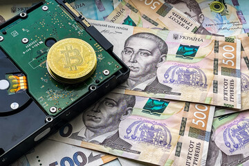 coins of Bitcoin on HDD and one thousand Ukrainian hryvnias. Electronic decentralized money concept.