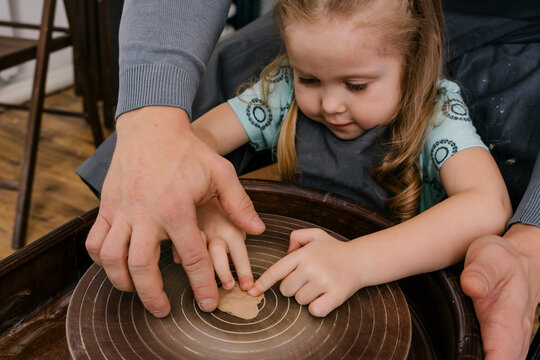 Man helping girl to mold mass in pottery wheel