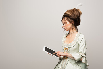 young woman in vintage dress using digital tablet with blank screen isolated on grey
