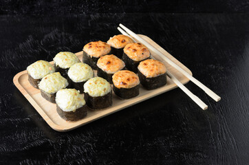 A set of seafood rice rolls wrapped with dried sea grass in a wooden platter on a black wooden background.