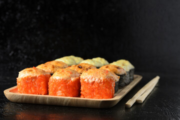 A set of various rolls with chopsticks in a wooden bamboo plate on a black wooden background.