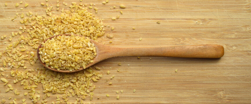 Cracked wheat daliya grains in wooden spoon, on bamboo cutting board
