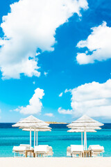 Obraz premium (Selective focus) Stunning view of some white thatch umbrellas and sunbeds on a white sand beach bathed by a beautiful, turquoise sea. Romazzino Beach, Porto Cervo, Sardinia, Italy.