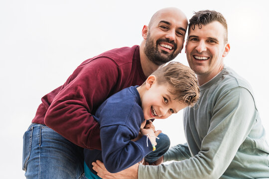 Happy gay male parents and son having fun playing outdoor in the city - Lgbt people and family love concept - Soft focus on boy face