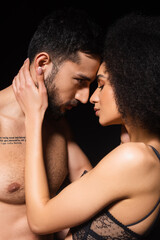 Fototapeta premium Side view of african american woman touching shirtless boyfriend isolated on black