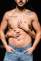 Naklejka premium Cropped view of woman scratching torso of sexy boyfriend on black background