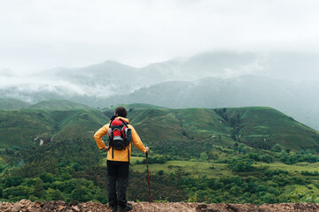 Hiker with yellow raincoat leaning on his trekking pole resting and contemplating the mountainous landscape with fog on a rainy day in Asturias, Spain. Mountain Sports